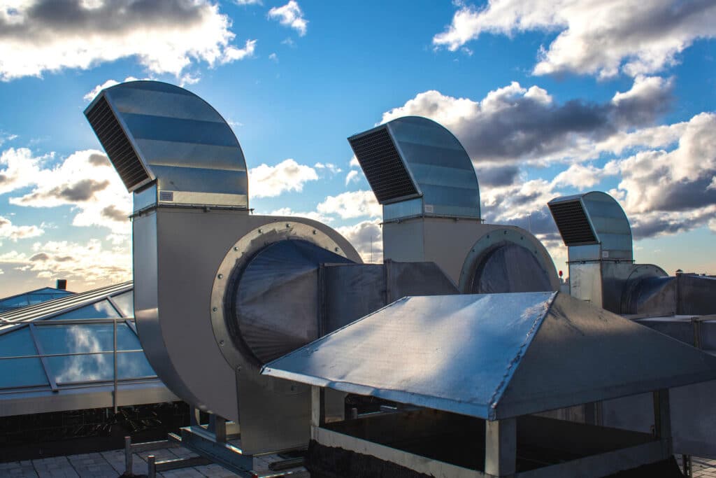 Industrial rooftop air vents against cloudy sky.