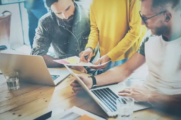 A team of WordPress web designers are huddled on a table discussing how a new project looks across laptop, tablet and phones.